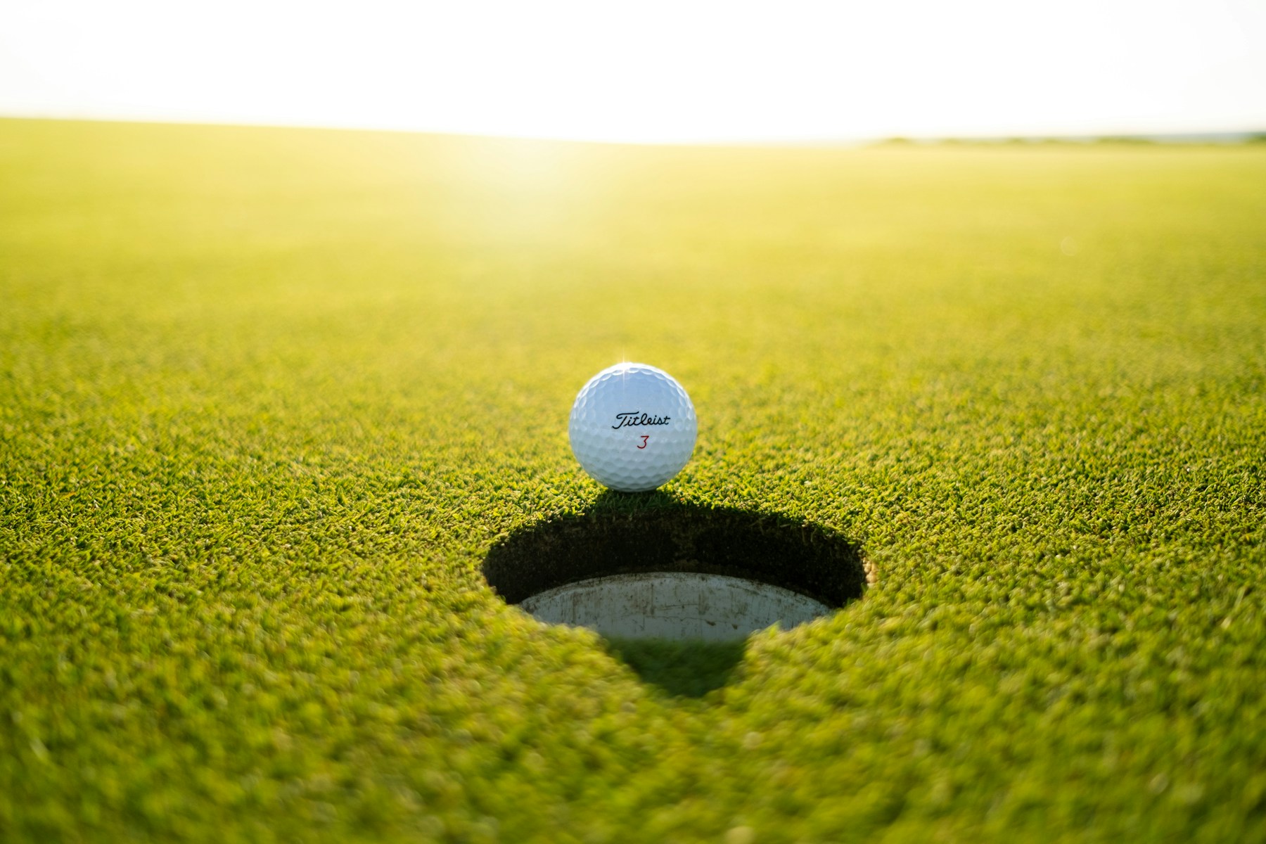 A golf ball resting beside the cup on a sunny green